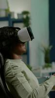 Vertical . Black woman gamer playing game at powerful computer late wearing vr headset. Excited player using wireless controller for virtual tournament gaming at home video
