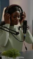 Vertical . African blogger smiling at audience while filming podcast, looking at camera putting on headset. On-air production internet broadcast host streaming live content, recording digital social media video