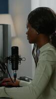 Vertical . Portrait of concentrated african gamer looking at camera smiling, playing online game for gaming tournament. Cyber performing on powerful pc with RGB keybord streaming videogames video