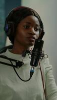 Vertical . African vlogger recording blog using smartphone with modern equipment in home studio podcast. Media star looking at camera for broadcast and having fun using technology to connect with audiences video