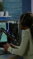 Vertical . Black woman streamer playing videogames with joystick talking with teammates on streaming open chat. Cyber performing on RGB powerful computer in gaming room using professional equipment video