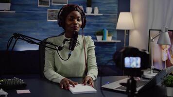 Black blogger influencer recording blog concept waving and speaking looking at camera on tripod in home podcast studio. Social media vlogger shooting vlog, streaming online broadcast video