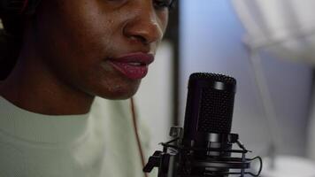 Close up of afro woman vlogger making new blog in home studio talking in professional microphone with audience. Speaking during livestreaming, blogger discussing in podcast wearing headphones. video