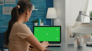 Back shot of freelencer working at marketing project using isolated pc with mock up green screen chroma key display. Woman typing on laptop computer sitting in home office studio video