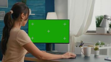 Business woman typing on professional computer with mock up green screen chroma key sitting at modern office desk. Female working at marketing project on pc with isolated display video