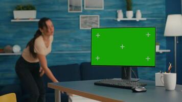 Woman lying on sofa reading a book in living room equipped with desktop computer with mock up green screen chroma key standing on table. Pc with isolated display is ready for online business video