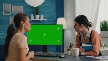 Two women looking at computer with mock up green screen chroma key working at business commerce. Office desk is equipped with isolated home office pc video