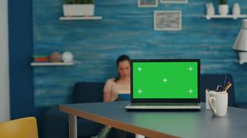 Laptop computer with mock up green screen chroma key standing on desk while in background two women talking about business commerce. Home studio is eqquiped with powerful isolated pc video
