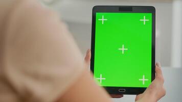 Close up of woman hands holding tablet computer with mock up green screen chroma key display. Freelancer sitting on office desk in living room working with isolated device for online lifestyle project video