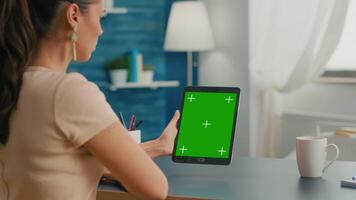 Freelancer woman working on communication ideas for online project using tablet computer with mock up green screen chroma key display. Office room in equipped with powerful isolated device video