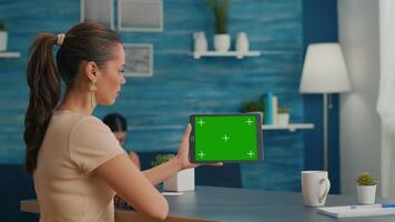 Woman looking at tablet computer with mock up green screen chroma key display browsing on internet searching lifestyle ideas. Freelancer using isolated device standing on desk office in living room video