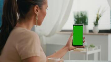 Over shoulder of business woman using isolated smartphone with mock up green screen chroma key sitting on table desk, while talking with her friends during online videocall sitting on office desk video