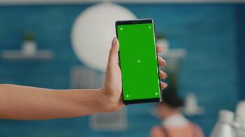 Hands of freelencer holding vertical mock up green screen chroma key smartphone. Business woman using isolated phone for browsing social networks sitting on office desk video