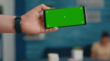 Front view of horizontal isolated mock up green screen chroma key display of modern phone. Two collegues talking about internet browsing and social media in home studio background video