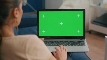 Close up of freelencer using laptop computer with mock up green screen chroma key display while sitting on sofa in living room., Woman working on personal business using isolated pc video