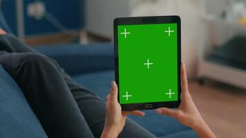 Close up of business woman hands holding tablet computer with mock up green screen chroma key display sitting on sofa. Freelancer using isolated touchscreen device for social networks browsing video
