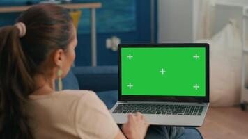 Caucasian female lying on sofa looking at laptop computer with mock up green screen chroma key display. Business woman working on financial graphs using isolated pc in home office video