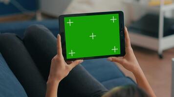 Close up of woman holding in horizontal mode tablet computer with mock up green screen chroma key display lying on sofa. Freelancer using isolated touchscreen device for social networks browsing video