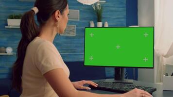 Business woman browsing on computer with mock up green screen chroma key display looking for online advertising sitting at desk table. Freelancer using isolated pc in home office video