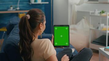 Business woman looking at tablet computer with mock up green screen chroma key display sitting on sofa in living room. Freelancer using isolated touchscreen device for social networks browsing video