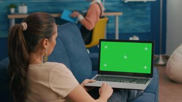 Freelancer sitting on couch working on business ideas using laptop computer with mock up green screen chroma key display. Caucasian female searching the network use isolated pc video