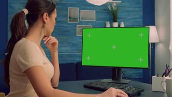Caucasian female searching on computer with mock up green screen chroma key display browsing on internet for business communication sitting at desk table. Freelancer using isolated pc in home office video