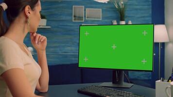 Freelancer woman at home sitting on desk table working on computer with mock up green screen chroma key display. Freelancer using isolated pc in home office for lifestyle opinions video