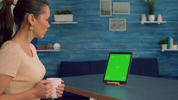 Freelancer looking at tablet computer display with mock up green screen chroma key while searching ideas on network. Caucasian female sitting on desk in office studio using powerful isolated gadget video