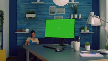 Freelancer working on powerful computer with mock up green screen chroma key display sitting on desk table. Caucasian female looking for business nformation on network using isolated pc video