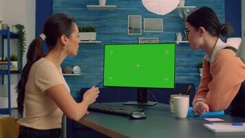 Two collegues working together on computer with mock up green screen chroma key display for social media advertising. Teammates looking at isolated pc sitting at desk table in home office video