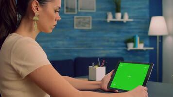 Freelancer reading online book using tablet computer with mock up green screen display sitting at office desk. Caucasian woman looking at template chroma key isolated device using technology internet video