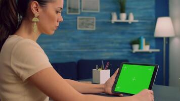 Woman working at office desk using mock up green screen tablet computer in landscape mode, watching online content. Freelancer looking at template chroma key isolated device using technology internet video