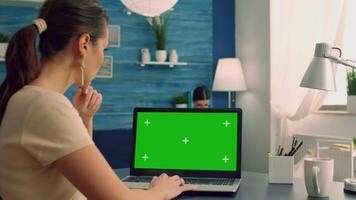 Freelancer looking at laptop computer with mock up green screen chroma key display sitting on desk table in office home. Business woman typing ideas for business commerce using isolated pc video