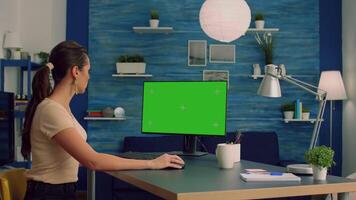 Teammates sitting on desk table while talking about business communication working on computer with mock up green screen chroma key display. Office desk is equipped with isolated home office pc video