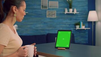 Freelancer woman browsing on internet business advertising using isolated device standing in home office studio. Caucasian female working with tablet computer with mock up green screen chroma key video