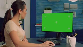 Freelancer sitting at desk table and browsing on network for commerce business using computer with mock up green screen chroma key. Caucasian female working with isolated pc in office home apartment video