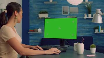 Business woman working on online advertising using computer with mock up green screen chroma key display sitting on table desk. Office room is equipped with isolated home office pc video