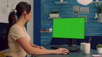 Caucasian female at her desk working on personal computer with mock up green screen chroma key display. Woman browsing on internet advertising for company business using isolated pc video