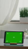 Vertical . Two collegues talking about internet connection in front of tablet computer with mock up green screen chroma key. Women browsing on isolated device sittings at office desk in modern living room video