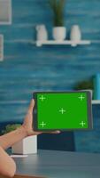 Vertical . Woman looking at tablet computer with mock up green screen chroma key display browsing on internet searching lifestyle ideas. Freelancer using isolated device standing on desk office in living room video