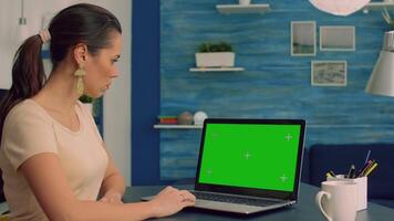 Freelancer working at business communication uses laptop computer with mock up green screen chroma key display. Caucasian female typing on isolated pc while sitting at desl table in home office video