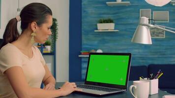 Business woman working at online coomunication project using laptop computer with mock up green screen chroma key display. Caucasian female standing on table desk working with isolated pc video