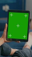 Vertical . Caucasian female lying on sofa having online meeting on tablet computer with mock up green screen chroma key display. Woman using isolated touchscreen device for social networks browsing video