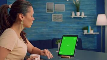 Business woman reading emails while drinking coffee sitting at office desk table in office home studio. Woman looking at template chroma key isolated tablet computer display using technology internet video