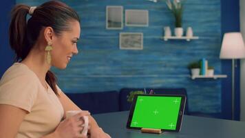 Freelancer holding touchpad with mock up green screen standing on office desk in living room. Woman looking at template chroma key isolated tablet computer display using technology internet video