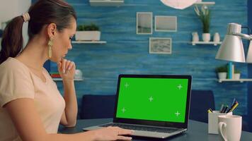 Caucasian female working at business comunication project on laptop computer with mock up green screen chroma key display. Freelancer sitting on desk in home office studio equipped with isolated pc video
