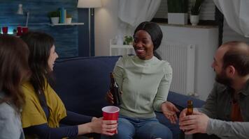 Woman with black skin gathering late at night with friends in living room sharing lifestyle advice while drinking beer. Group of mixed race people hanging out enjoying time spending together video