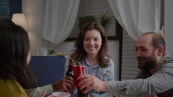 Multiethnic friends gathering late at night in living room while resting on sofa cheering beer bottles during home party. Group of mixed race people hanging out enjoying time spending together video