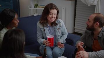 Group of multi-ethnic happy friends having fun during entertainment wekeend party drinking beer, eating snack while relaxing on sofa. Mixed race people hanging out enjoying time spending together video