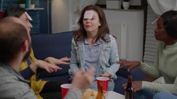 Multiracial friends enjoying friendship while playing guess who game attaching sticky notes on forehead. Mixed race people having fun, laughing together while sitting on sofa late at night video